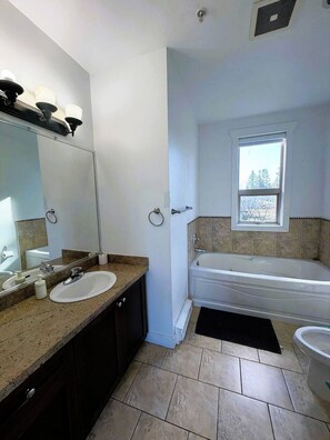 A bathroom with a sink, mirror, bathtub, and window. - Modern & Spacious 3BR Apartment in Surrey (Surrey)