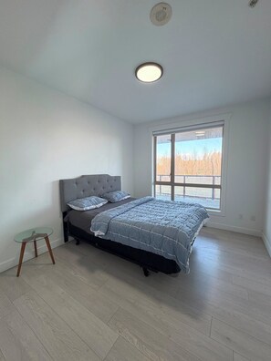 A bedroom with a bed, a small table, a window with a view, and a ceiling light. - Modern & Spacious 3BR Apartment in Surrey (Surrey)