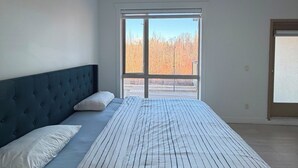 Quarto com cama grande, janela com vista para árvores e luminária no teto.