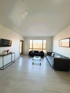 A spacious living room with a sofa, a coffee table, and a TV mounted on the wall. - Modern & Spacious 3BR Apartment in Surrey (Surrey)