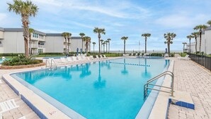 Une piscine entourée de chaises longues, de palmiers et d’un bâtiment doté de balcons.
