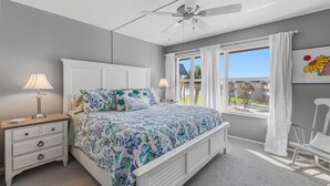 Une chambre à coucher avec un lit, des tables de chevet, un ventilateur de plafond et une fenêtre avec des rideaux.