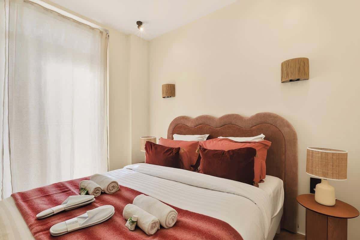 A hotel room with a bed, pillows, a nightstand, a lamp, and towels.