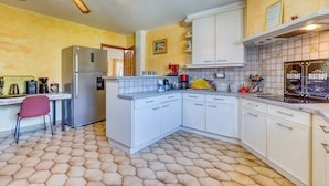 A kitchen with white cabinets, a refrigerator, a coffee maker, and a dining area with a chair.
