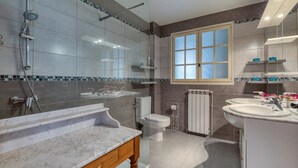 A modern bathroom with a glass shower enclosure, a marble vanity, a toilet, and a window with frosted glass panes.