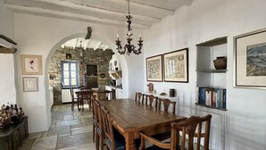 Un vaste espace dédié à la salle à manger, avec une longue table en bois et des chaises, un sol en pierre et une cheminée en pierre en arrière-plan.