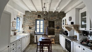 Une cuisine avec des meubles blancs, un mur en pierre, une table en bois et un sol en pierre.