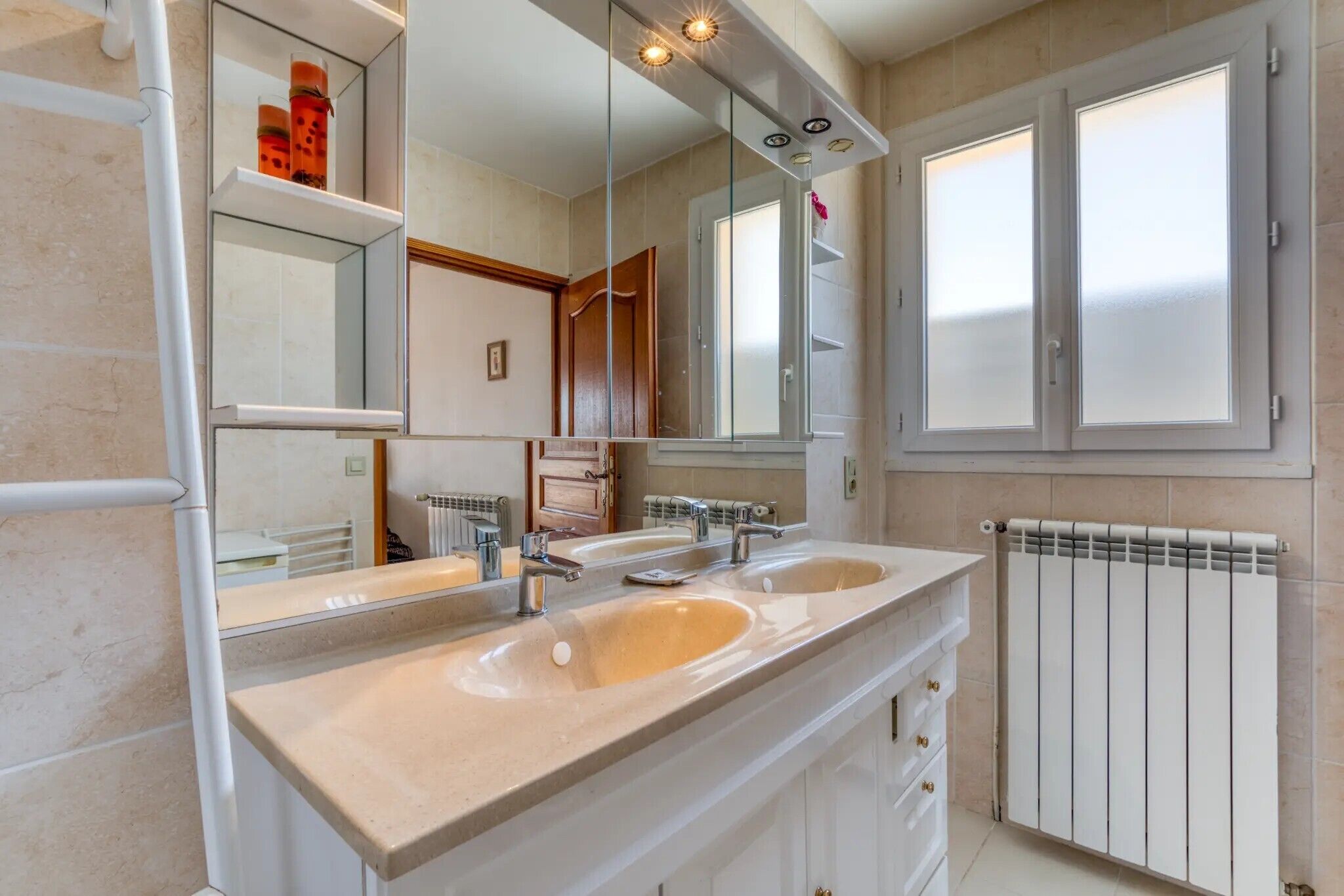 Un bagno moderno con doppio lavabo, un ampio specchio e un termosifone.