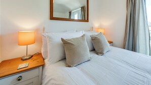 A hotel room with a bed, two bedside lamps, a nightstand with a remote control, a wooden headboard, and a large mirror. - Cosy 3BR House with free parking (Oxford)