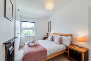 Ein Schlafzimmer mit Bett, Nachttischen, Heizkörper, Fenster und einer Pendelleuchte.