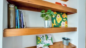 A shelf with books, a potted plant, a colorful card, and a metal container. - Cosy 3BR House with free parking (Oxford)