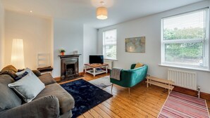 A living room with a fireplace, a sofa, a television, and a large window with blinds. - Cosy 3BR House with free parking (Oxford)