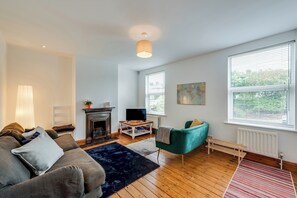 A living room with a fireplace, a sofa, a television, and a large window with blinds. - Cosy 3BR House with free parking (Oxford)