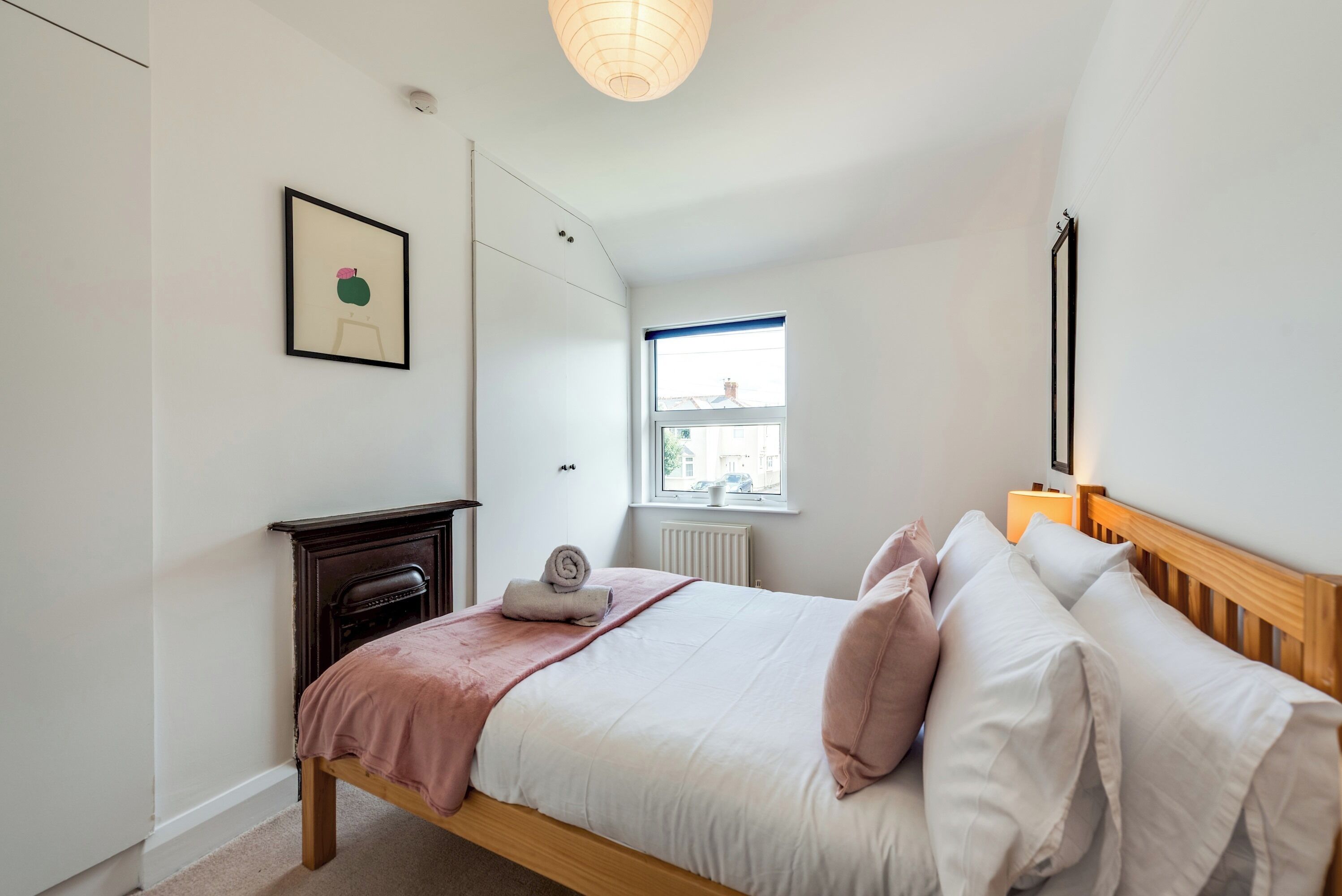 A bedroom with a bed, a bedside table, a window, and a framed picture on the wall.