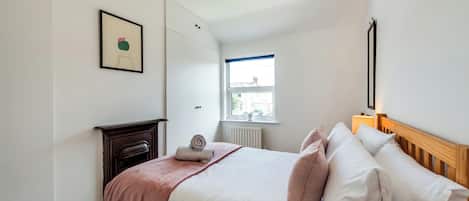 Un dormitorio con una cama, una mesita de noche, una ventana y un cuadro en la pared.