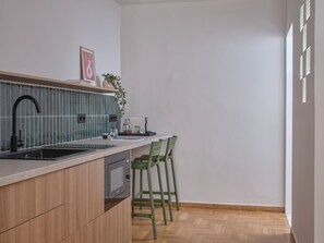 A modern kitchen with a built-in microwave, a sink, and a wooden countertop. There are two green chairs and a small table with a plant and a framed picture on the counter. - Two Bedroom Apartment (Athina)