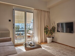 Ein Wohnzimmer mit einer Couch, einem Couchtisch, einem Fernseher, einer Schiebetür aus Glas und einer Topfpflanze.
