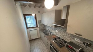 Eine Küche mit Gaskochfeld, Backofen und Toaster, ein Fenster mit Vorhängen und eine Heizung.