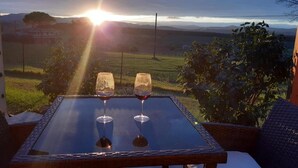 Ein Tisch mit zwei Weingläsern und Blick auf den Sonnenuntergang über einem Weinberg.