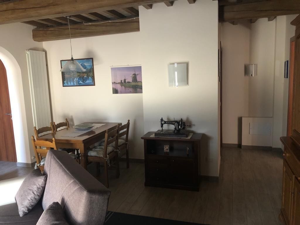 Ein Zimmer mit Holzbalkendecke, einem Esstisch mit Stühlen, einer Nähmaschine und zwei gerahmten Bildern an der Wand.