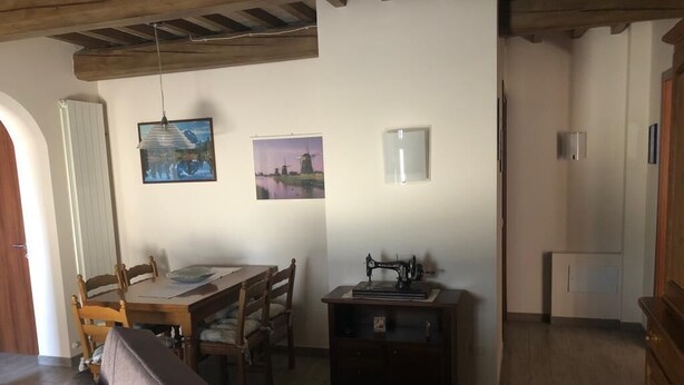 Ein Zimmer mit Holzbalkendecke, einem Esstisch mit Stühlen, einer Nähmaschine und zwei gerahmten Bildern an der Wand.