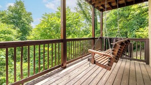 Eine Holzterrasse mit einer Schaukel, umgeben von einem Geländer, mit Blick auf ein bewaldetes Gebiet.