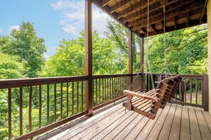 A wooden deck with a swing chair, surrounded by a wooden railing, overlooking a forested area. - 🏔️ Rendez-View | 4BR Mountain Escape | Theater, Game Room & Hot Tub | Sleeps 12 (Sevierville)