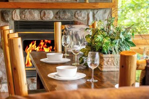 A wooden dining table set with white bowls and wine glasses, a fire in the background, and a potted plant with green foliage. - 🏔️ Rendez-View | 4BR Mountain Escape | Theater, Game Room & Hot Tub | Sleeps 12 (Sevierville)