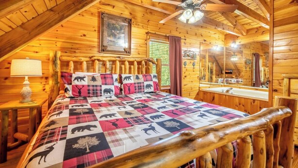 Ein Schlafzimmer im Holzblockhausstil mit einem Bett, einem Deckenventilator, einem Fenster und einem Spiegel.