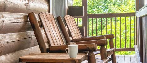 A wooden porch with a table and two wooden chairs.