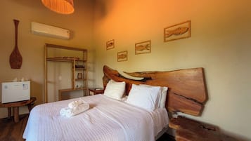 A bedroom with a wooden headboard, a bed with white bedding, a wooden nightstand, a wall-mounted air conditioner, and a wooden shelf with decorative items.