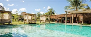 Una zona de piscina con sillones reclinables y una estructura de techo de paja.