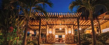 Un espacio exterior techado con un muro de piedra, una pérgola de madera y una piscina.