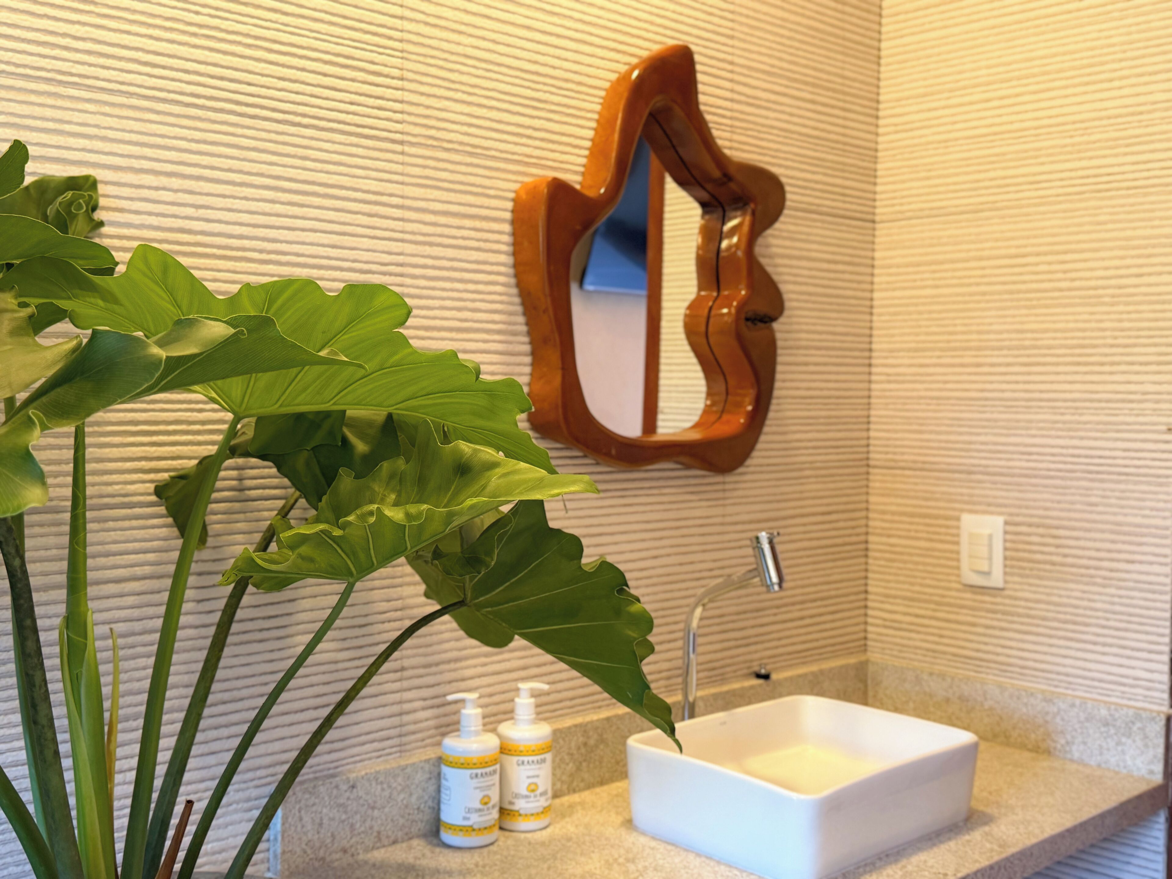 A bathroom with a white sink, a wooden mirror, and a large green plant.