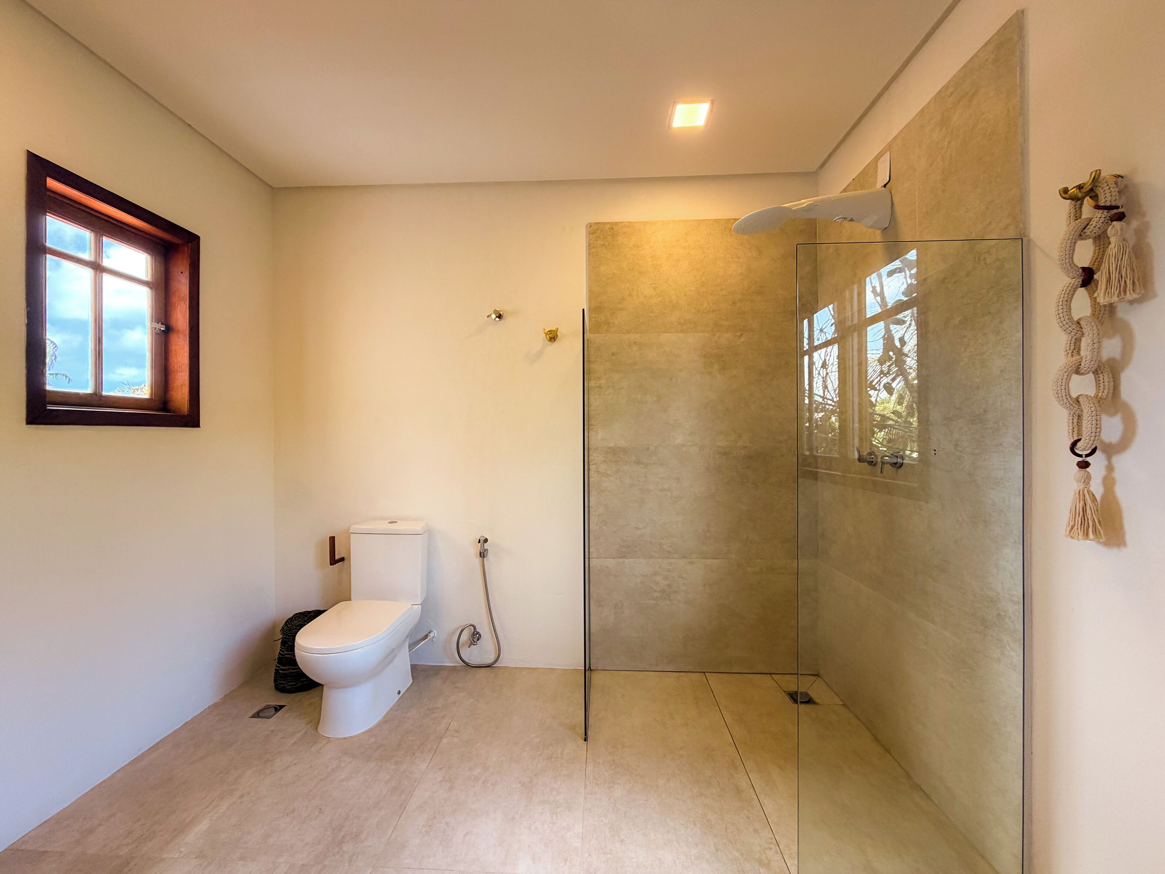 A bathroom with a toilet, a shower with a glass door, and a window with a view.