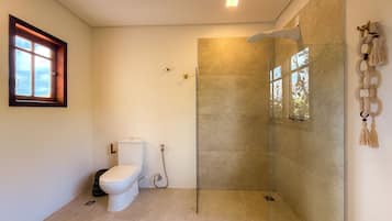 A bathroom with a toilet, a shower with a glass door, and a window with a view.