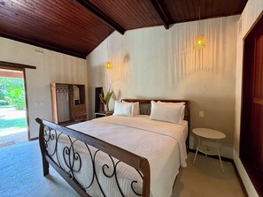 Un dormitorio con estructura de cama de madera, una mesita de noche, un espejo y una pequeña mesa redonda.