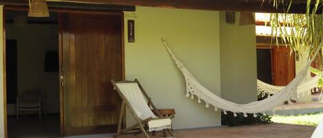 A wooden door, a hammock, and a chair outside a building.