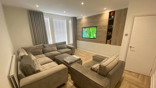 Een moderne woonkamer met een hoekbank, een flatscreen televisie en een houten vloer met een herringbone-patroon.