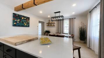 Een moderne keuken met een groot kookeiland, houten balken in het plafond, inbouwverlichting en een eethoek met een plant.