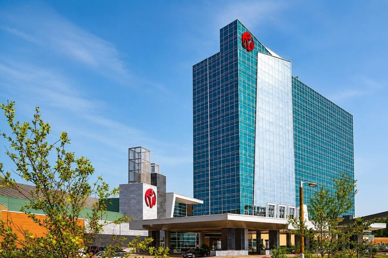 A modern hotel with a prominent glass facade, a central entrance, and a clear sky.