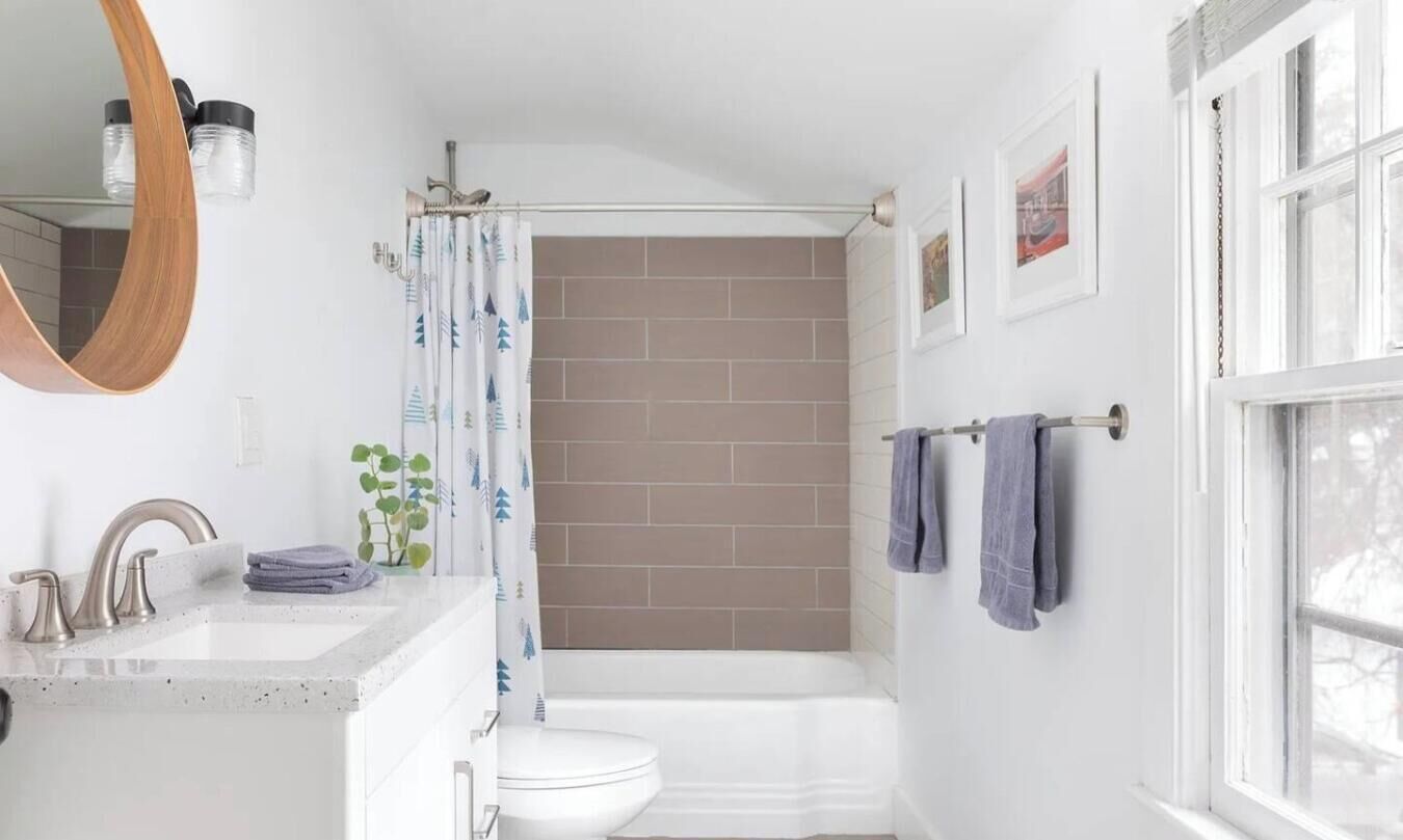Un baño con un lavabo blanco, un inodoro, una bañera y una cortina de ducha. Hay toallas colgadas en un perchero y un espejo sobre el lavabo.