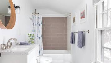 Un baño con un lavabo blanco, un inodoro, una bañera y una cortina de ducha. Hay toallas colgadas en un perchero y un espejo sobre el lavabo.