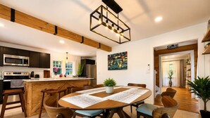 Cozinha moderna com ilha central, armários de madeira e área de refeições com mesa redonda e cadeiras.