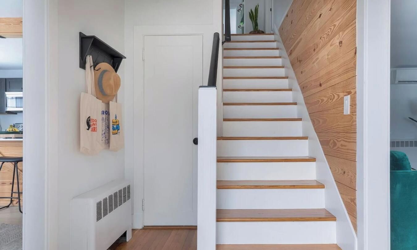 Una escalera con escalones blancos y barandillas de madera que lleva a una habitación con una puerta blanca y un radiador.