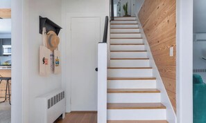 Una escalera con escalones blancos y barandillas de madera que lleva a una habitación con una puerta blanca y un radiador.