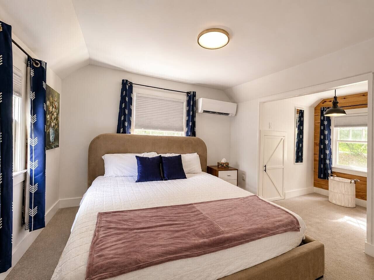 Een slaapkamer met een groot bed, een nachtkastje, een airconditioningapparaat, een raam met gordijnen en een deur.