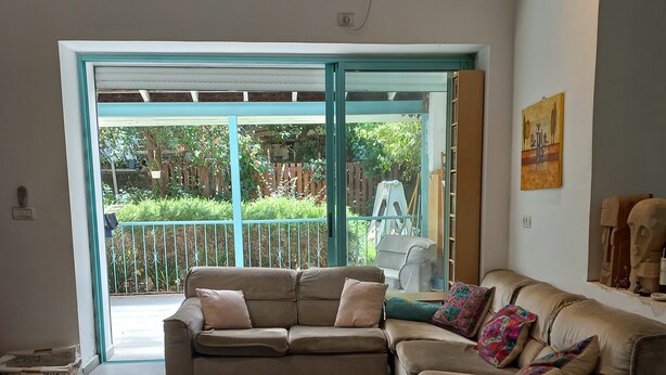 Ein Wohnzimmer mit einem beigefarbenen Ecksofa, einem Streifenmuster-Teppich und einer Glastür, die zu einem Garten führt.
