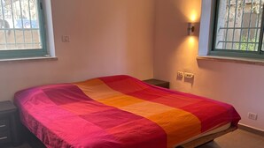 Ein Einzelbett mit farbenfroher Decke, ein Nachttisch, eine Steckdose und ein Fenster mit Blick.