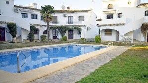 A swimming pool with a stone border, surrounded by a grassy area and a building with multiple balconies and windows. - Ap1139 in Denia With 1 Bedrooms and 1 Bathrooms (Denia)